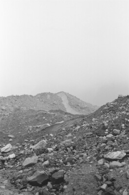 Fractured Landscape, 2019. Black-and-white analogue photograph showing a rocky landscape resting on glacier ice, divided by a visible crack through the ground.