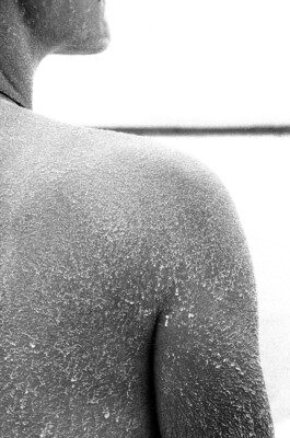 The Crystal Carpet on My Skin, 2019. Black-and-white analogue photograph showing a close view of a shoulder and upper body covered with fine crystalline salt traces.