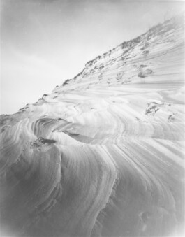 Analog black-and-white photograph of a steep sand valley on the Curonian Spit, showing layered wind-shaped ridges and sparse vegetation.