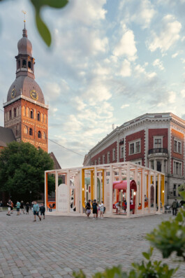 Dome Next Door, 2024, urban art installation in Riga Old Town, Latvia, with people gathering around and using the timber pavilion beneath Riga Cathedral tower.