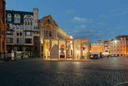 Evening view of Dome Next Door, 2024, illuminated within Riga Old Town, Latvia, showing the timber urban art installation in the historic public square.