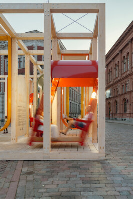 Motion-blurred red swing seating in use within Dome Next Door, 2024, a timber urban art installation in Riga Old Town, Latvia.