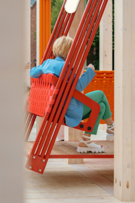 Person seated on a red suspended swing within Dome Next Door, 2024, an urban art installation in Riga Old Town, Latvia.